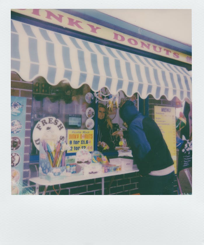 A nostalgic instant film photo of a street vendor selling donuts to a customer.