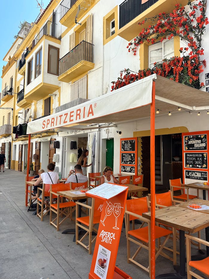 Colorful cafe patio with people dining outdoors in a sunny cityscape.