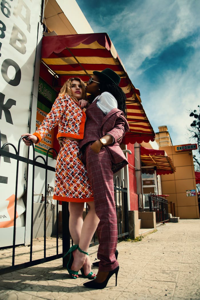 Two fashionable women pose stylishly outdoors in a vibrant urban setting.